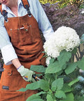 Person gardening while wearing rugged leather welding apron with eleven tool pockets for woodworking and metalworking.