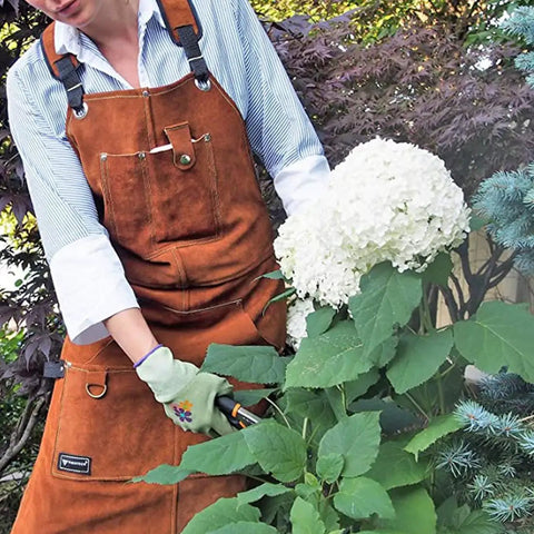 Person gardening while wearing rugged leather welding apron with eleven tool pockets for woodworking and metalworking.