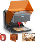 Genmitsu laser engraver with orange hood and gray body; 3.9x3.9 in engraving area; shown with mug, wallet, wood panel.