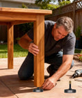 Man adjusting Sturdy True Metric M8 Heavy Duty Leveling Feet with a 2 inch wide base under a wooden table outdoors