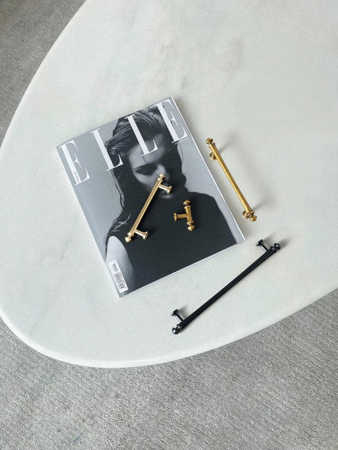 Gold and black cabinet pulls resting on a magazine and table, showcasing a variety of finishes and styles for interior design.