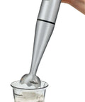 Slick 200 Watt Immersion Hand Blender With Brushed Stainless Steel Build blending ingredients in a clear beaker.