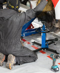 Kaflla High Lift Hydraulic Transmission Jack 1660 Lb With Foot Pedal being used by a mechanic kneeling beneath a vehicle.