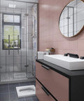 Modern bathroom with glass shower, pink tiles, black vanity, and round mirror.