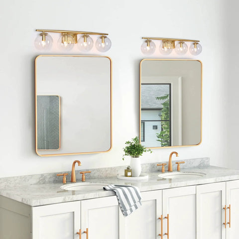 Gold Vanity Light Fixture For Bathroom Over Mirror With Four Lights, Clear Globe Glass Shades, installed above dual sinks.