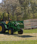 Tractor with light-duty fork stabilizer bar lifting pallet, preventing fork spread, use with bales and logs. Adjustable clamp-on 3x2 inch.
