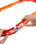 Hands assembling orange track from Track Builder Unlimited Playset Premium Curve Pack With 16 Component Parts And 1 64 Scale Vehicle.
