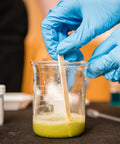 Gloved hands stirring liquid in a 250ml low-form glass beaker from 3 Piece Glass Beaker Set Lab Gear With 50ml 100ml 250ml Low Form Borosilicate 3.3 Lab Grade Beakers Featuring Double Scale For Pro Level Chemistry Experiments And Easy Measurement