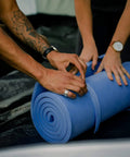 Hands rolling up the Pack Lite Camping and Backpacking Sleeping Pad Lightweight Closed Cell Foam Mat for Outdoor Sleep Waterproof and Puncture Proof Roll Up Design With Straps Keeps You Dry and Cozy From Cold and Dampness on Hikes and Trips.