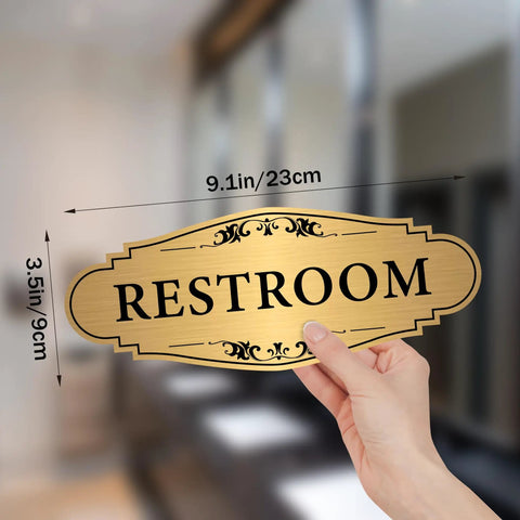 Hand holding Gold Brushed Restroom Sign Sticker For Business And Home Self Adhesive Waterproof Bathroom Door Sign Unisex