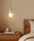 Wabi Sabi Travertine Pendant Light with Wood Ball & Milk Glass Shade hanging above a wooden nightstand in a cozy bedroom.