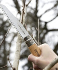 Badass Lightweight Folding Saw For Weekend Campouts And Garden Grind Cuts Branches Fast With Razor Sharp Carbon Steel Blade Secure Virobloc Lock And Natural Beechwood Handle cutting through a branch.