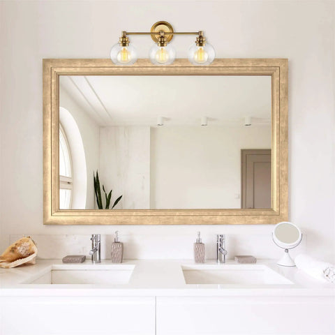 22 Inch Modern Three Light Vanity Bathroom Light With Clear Glass Globe Shades And Warm Brass Finish For Rustic Farmhouse Vibe And A Sharp Stylish Powder Room Glow mounted over a double sink bathroom mirror
