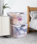 Hella Spacious 90 Quart Clear Plastic Storage Bins With Tight Lids 8 Pack stacked with clothes beside a bed for home organization.