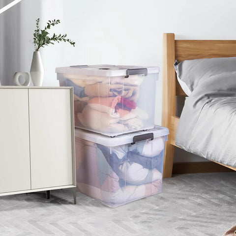 Hella Spacious 90 Quart Clear Plastic Storage Bins With Tight Lids 8 Pack stacked with clothes beside a bed for home organization.