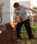 Man using heavy duty garden shovel for digging and trenching, scoop spade hoe tool with orange handle in a garden.