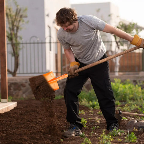 Man using heavy duty garden shovel for digging and trenching, scoop spade hoe tool with orange handle in a garden.