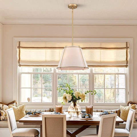 3 Light Gold Pendant Light Featuring White Linen Cone Shade And Sturdy Metal Cage hanging above a dining table in a farmhouse setting.