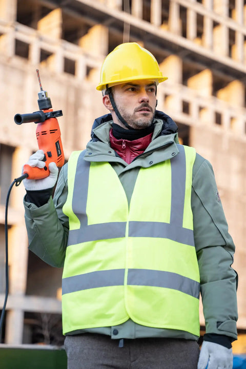 Look Sharp Hi Vis Safety Vest With Wraparound 360 Reflective Strips For Construction Crews Road Work Cycling And After Dark Jogging Activities Reliably worn by man holding drill