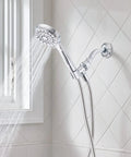 Ignite Chrome Handheld Shower System with modern sleek design and mirror-like finish spraying water by a window