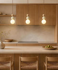 Wabi Sabi Travertine Pendant Light with Wood Ball & Milk Glass Shade above a kitchen island with wooden cabinetry.