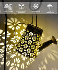 Solar Powered Watering Can Lantern With LED Lights For Garden Decor casting floral patterns at night on a shepherd hook.