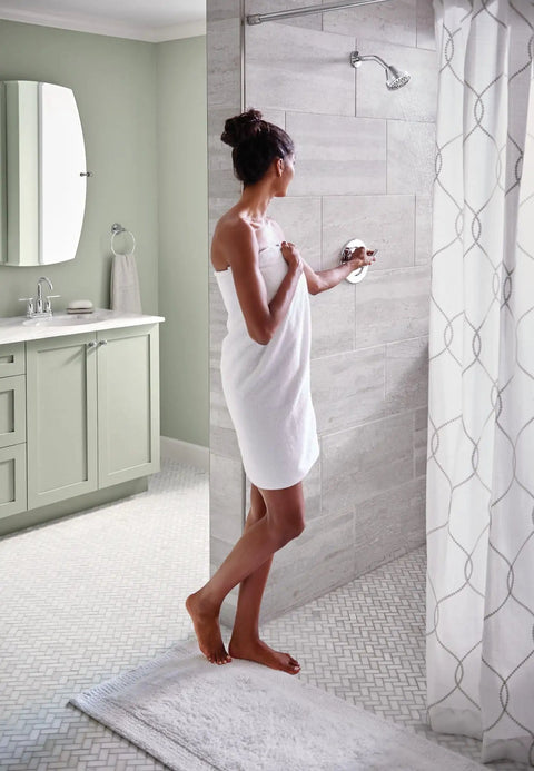 Person in bathroom using Gibson Chrome Posi Temp Shower Trim With Pressure Balancing Eco Performance, tiled shower visible