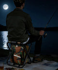Person fishing at night using Foldable Camping Chair Backpack With Built In Cooler Insulated Picnic Bag, moonlit setting