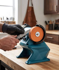 Daconovo 3 Inch Cordless Mini Bench Grinder With Dual 5500Rpm Wheels, sharpening a knife on the orange wheel in a workshop.