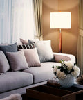Lucas LED Floor Lamp With Drum Shade And Warm Wood Finish beside a sofa in living room.