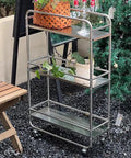 Slick Rolling Kitchen Island Trolley With Ample Storage Shelves And Quiet Locking Wheels For Mobile Coffee Bar Station Or Heavy Duty Stainless Steel Tool Caddy Rig in outdoor setting with plants.