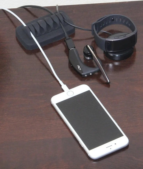 Must Have Weighted Desktop Cable Organizer That Keeps Cords Tidy All Day Heavy Duty Cord Holder Eco Friendly Silicone No Odor Includes Four Reusable Cable Ties Black on desk with smartphone and smartwatch.
