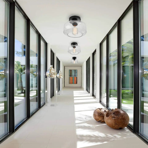 Heavy Duty Industrial Semi Flush Mount Ceiling Light With Tough Matte Black Frame And Authentic Seeded Glass Cover For A Big Time Modern Vintage Lighting Glow in a bright hallway.