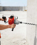 Kickass 25.4cc Gasoline Punch Drill And Concrete Breaker Kit used for chiseling concrete wall, showcasing the sharp tungsten bit in action.