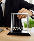 Five Ball Newton's Cradle Desk Toy For Gravity Demonstrations And Stress Relief, in use on an office desk