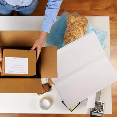Person using 100 Sheets Newsprint Packing Paper for Moving and Shipping on a table with packing materials and cardboard box
