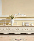 Elegant cream-colored cabinet with decorative drawers and crystal knobs, styled with floral arrangement and vases.