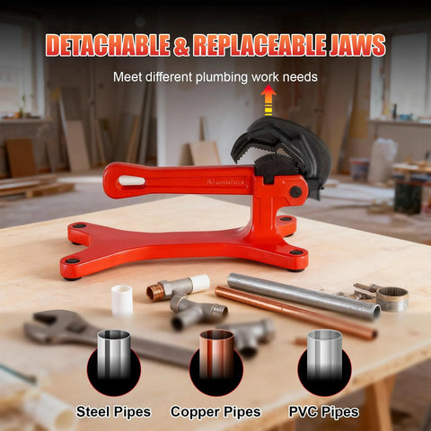 Front view of red aluminum portable pipe vise with black non-slip jaws on a workbench; copper and steel pipes nearby.