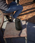 Revolve Plus II Portable Bluetooth Speaker With 360 Degree Sound And Built In Microphone on outdoor chair, showing carry handle.