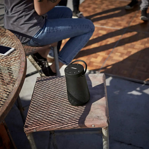 Revolve Plus II Portable Bluetooth Speaker With 360 Degree Sound And Built In Microphone on outdoor chair, showing carry handle.