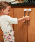 Child interacting with cabinet secured by Adhesive Baby Proof Straps Locks Pack Of 10 No Drilling Required For Cabinets Drawers Fridge Dishwasher.