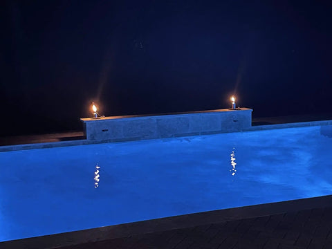 Night view of a poolside with two Polished Stainless Steel Table Top Tiki Torch Canister With Refillable Fuel Reservoir For Outdoor Use