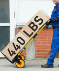 Folding hand truck dolly with yellow frame and orange wheels carrying cardboard boxes.