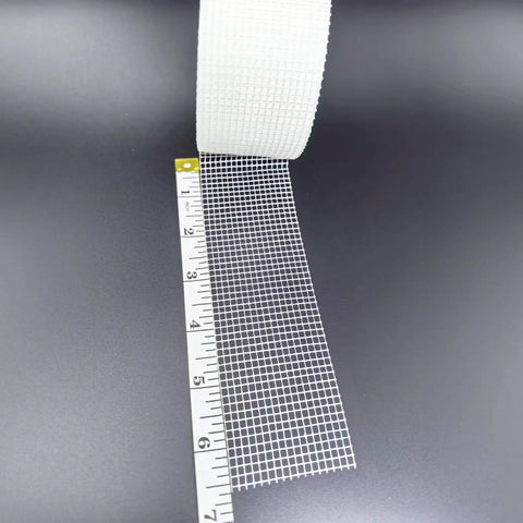 Fiberglass Drywall Repair Tape Self Adhesive Mesh, 2 Inch by 100 Ft Roll next to measuring tape, showing mesh size and texture