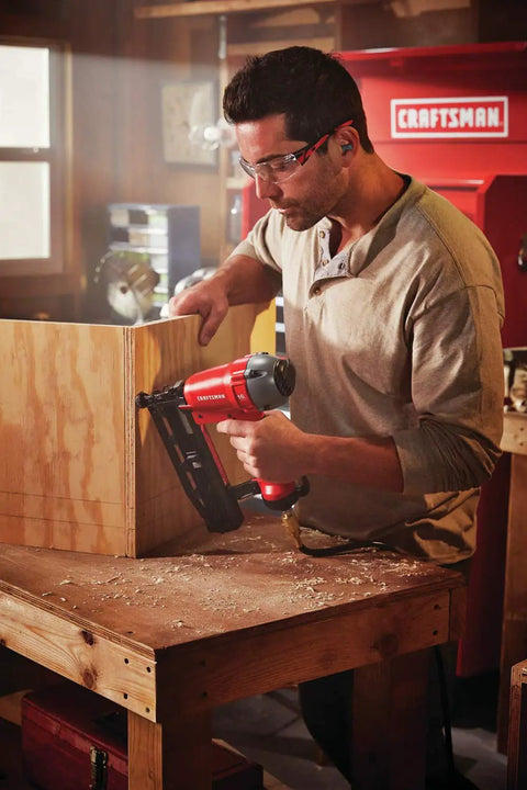 Carpenter using Finish Nailer 16 Gauge Pneumatic With Oil Free Motor in workshop on wooden project.