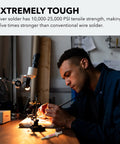 Person using Silver Solder Paste 7.1 Grams For Electronics Jewelry And Home Wiring No Mess on a workbench, microscope visible.