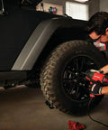Mechanic using half inch corded impact wrench 7.5 amp power 450 ft lbs max torque 2700 IPM on car tire in garage