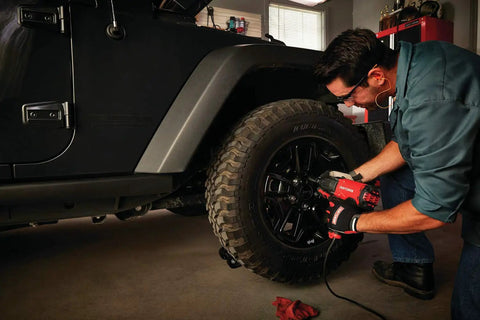 Mechanic using half inch corded impact wrench 7.5 amp power 450 ft lbs max torque 2700 IPM on car tire in garage