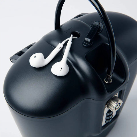Close-up of a portable indoor outdoor lock box safe with steel cable, key and combination access, headphones resting on top.