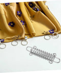 Image of a 3 Piece Adjustable Rope Buckle High Strength Spring Tensioner Set placed beside a floral decorated yellow fabric.